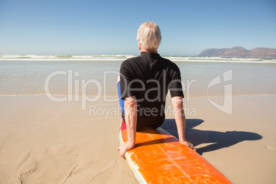 Rear view of senior man sitting on surfboard