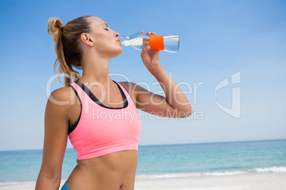 Woman drinking water while standing at beach