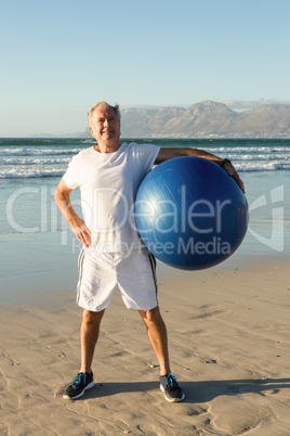 Portrait of senior man holding exercise ball while standing at beach
