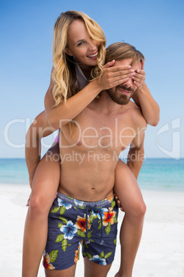 Man piggybacking cheerful woman at beach