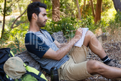 Man writing on notepad while resting on tree trunk