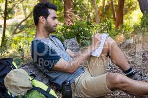 Man writing on notepad while resting on tree trunk