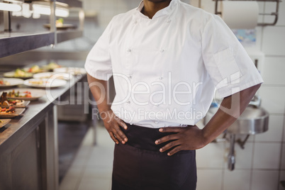Mid section of chef standing with hands on hip in commercial kitchen