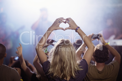 Rear view of woman making heart shape while enjoying at nightclub