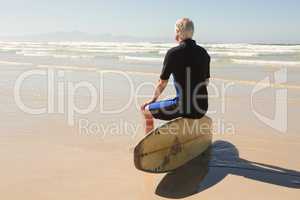Rear view of senior man sitting on surfboard