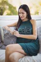 Woman using mobile phone while relaxing on sofa