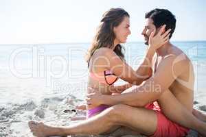 Side view of young couple sitting face to face on sand at beach