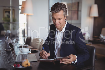 Smiling businessman writing on diary