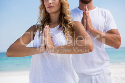 Midsection of couple in praying position exercising at beach