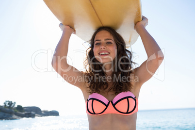 Portrait of smiling young woman carrying surfboard at beach