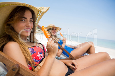 Portrait of female friends holding popsicles while sitting on deck chair