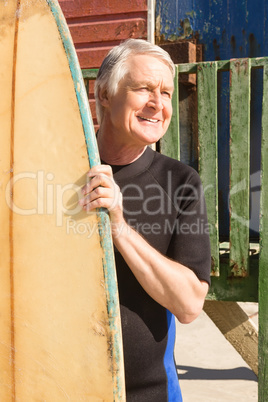 Happy man holding surfboard while standing against beach hut