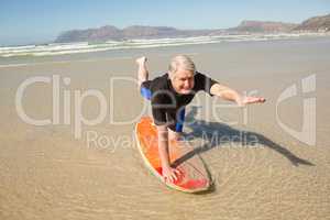 Senior man exercising on surfboard at shore