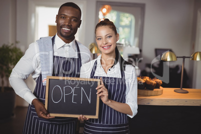 Smiling waiter and waitress showing chalkboard with open sign