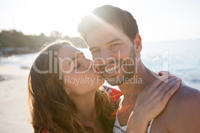 Portrait of smiling man being kissed by his girlfriend at beach