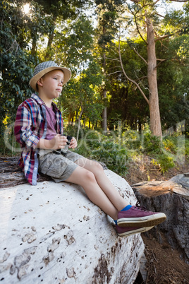 Boy with binoculars sitting in the forest