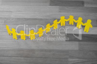 Yellow paper cutout human chain on wooden table