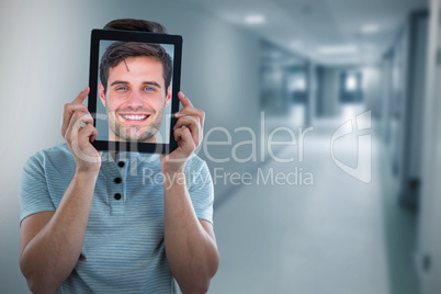 Composite image of man holding digital tablet in front of face