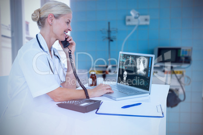 Composite image of smiling doctor using laptop while talking on telephone