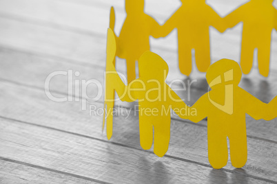 Yellow paper figures holding hands on wooden table