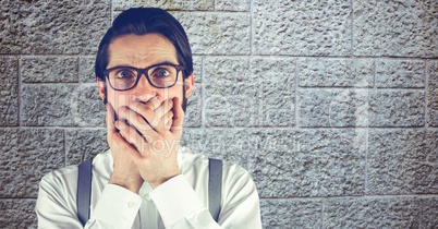 Shocked hipster covering mouth with hands against wall