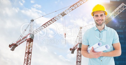 Smiling architect holding blueprints against cranes