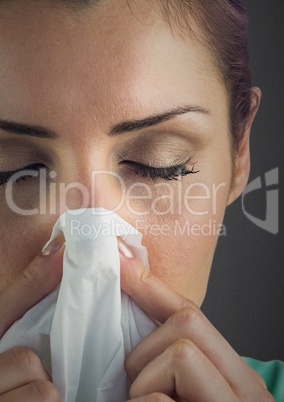 Close up of woman blowing nose against grey wall