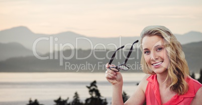 Happy woman holding eyeglasses with lake and mountains in background