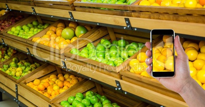 Hand photographing fruits and vegetables on smart phone in store