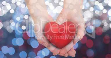 Female's hands holding heart shape over glowing bokeh