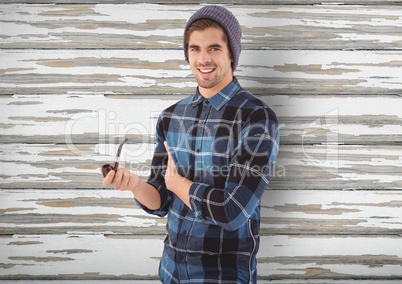 Smiling hipster holding smoking pipe over wooden wall