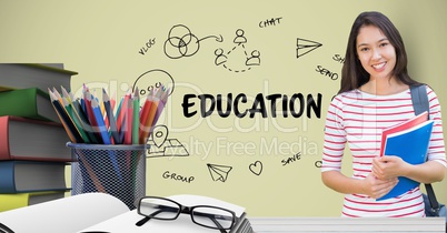 Female student holding books at table against education graphics