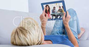 Woman video conferencing on tablet PC while lying on sofa