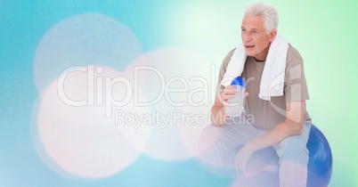 Fit senior man holding water bottle on ball by bokeh