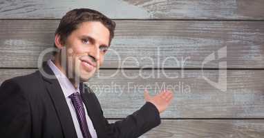 Portrait of smiling businessman gesturing towards wooden wall