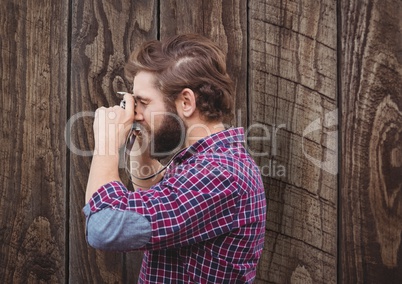 Side view of male hipster photographing against wooden wall