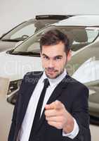 Salesman pointing against cars in showroom