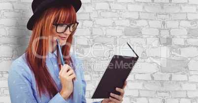 Female hipster reading book against wall