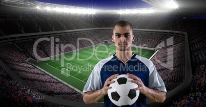 Confident player holding soccer ball against stadium