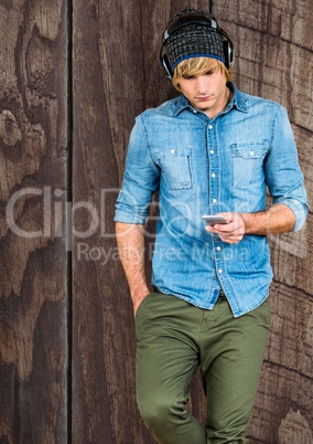 Male hipster using smart phone against wooden wall
