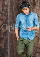 Male hipster using smart phone against wooden wall
