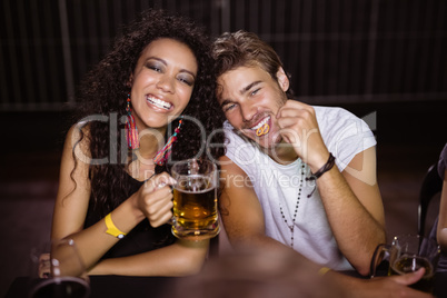 Portrait of smiling friends with beer mugs sitting at nightclub