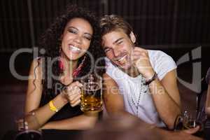 Portrait of smiling friends with beer mugs sitting at nightclub