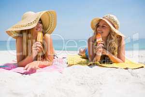 Female friends holding popsicles while lying on sand