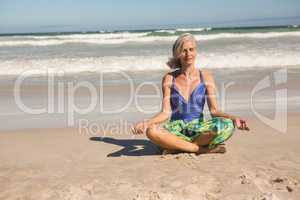 Senior woman meditating while sitting against sea