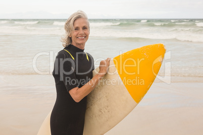 Portrait of smiling woman carrying surboard while standing on shore