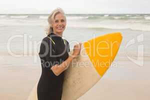 Portrait of smiling woman carrying surboard while standing on shore