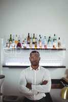 Portrait of bar tender standing with arms crossed at bar counter