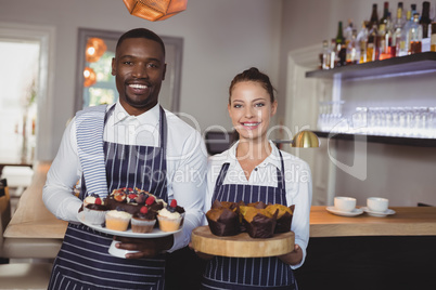 Smiling waiter and waitress holding desserts at counter
