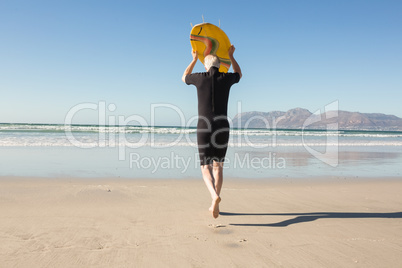 Rear view of senior man carrying surfboard at beach